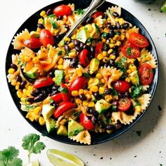 a black bowl filled with pasta salad next to cilantro and lime wedges