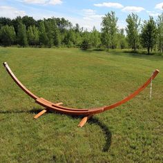 a wooden hammock sitting in the middle of a grassy field next to trees