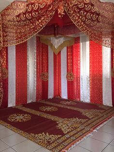 an elaborately decorated bed with red and white drapes on the sides, in a room