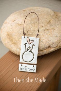 a wooden sign that says let it snow with a bunny hanging from the front on a rock