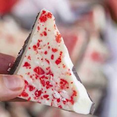 someone is holding a piece of cake with white frosting and red sprinkles