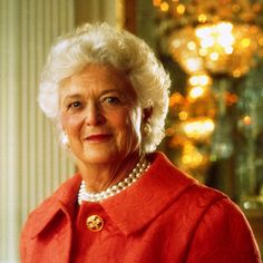 an older woman wearing a red coat and pearls