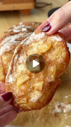 a person holding up a donut covered in powdered sugar and apple toppings