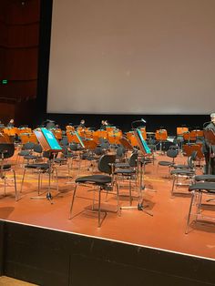 an orchestra performing on stage in front of a projector screen with chairs and music instruments