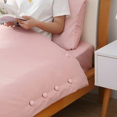 a woman reading a book in bed with pink sheets and pillows on the side table