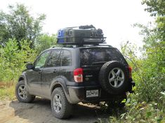 a black suv parked on the side of a dirt road with luggage strapped to it's roof