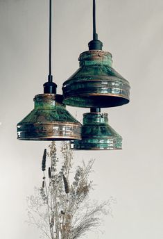 three green lights hanging from a ceiling over a vase with flowers in it and dried plants below