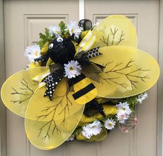 a yellow and black mesh wreath with flowers on the front door, featuring a bee