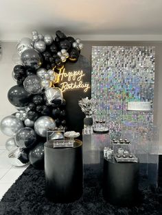 a birthday party with black and silver balloons on the wall, gifts in front of it