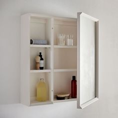 an open medicine cabinet with bottles and dishes on it's shelf, next to a mirror