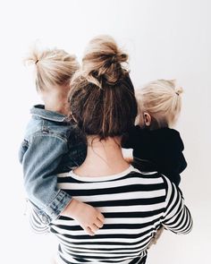 a woman holding two small children while they both have their arms around each other's shoulders