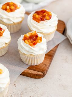 cupcakes with white frosting and fruit toppings on a cutting board next to plates