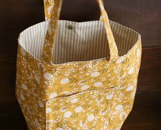 a yellow and white flowered bag hanging on a wooden wall with the handles down