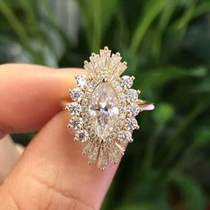 a person is holding a ring with an oval shaped diamond surrounded by smaller round diamonds