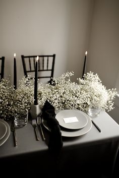 the table is set with black and white flowers in vases, silverware, and candles