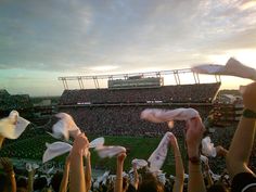 many people are holding up white paper towels in front of an empty football stadium as the sun sets