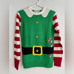 a green and red christmas sweater with candy canes on the chest hanging from a white wall