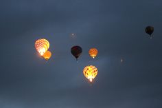 several hot air balloons flying in the sky at night, with one balloon glowing brightly