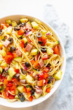 a bowl filled with pasta and vegetables on top of a white table next to a fork