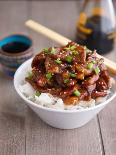 two chopsticks sticking out of a bowl of rice with meat and vegetables on top