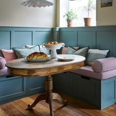 a table with bread and fruit on it in front of blue painted walls, along with two benches