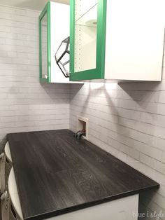 a kitchen with white brick walls and green cabinet doors on the back wall, along with a black counter top