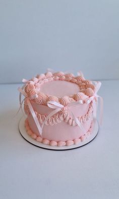 a pink cake sitting on top of a white plate covered in icing and ribbon