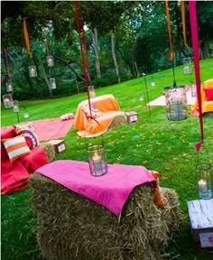 an outdoor setting with hay bales and pink linens on the grass, lanterns hanging from trees