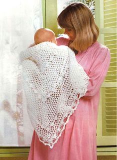 a woman holding a baby wearing a white crochet shawl over her shoulder