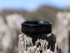 a black ring sitting on top of a piece of wood in front of some rocks