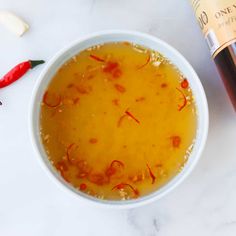 a white bowl filled with orange liquid next to a bottle of wine on a table