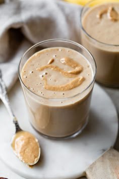 two glasses filled with peanut butter on top of a white plate next to spoons