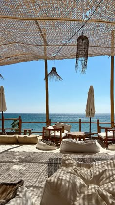 an outdoor area with lots of pillows and umbrellas over looking the ocean on a sunny day