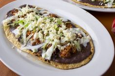 two tacos with meat, cheese and vegetables on them sitting on a white plate