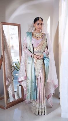 a woman in a white and blue sari standing next to a mirror with her hands on her hips