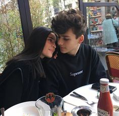 a young man and woman sitting at a table in front of a window looking into each other's eyes