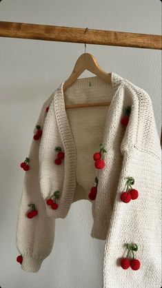 a white sweater with cherries on it hanging from a wooden hanger next to a wall