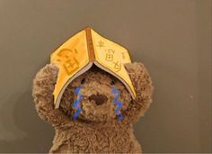 a brown teddy bear wearing a yellow hat with chinese characters on it's face