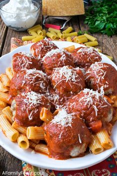 a white plate topped with pasta and meatballs covered in marinara sauce, cheese and parmesan