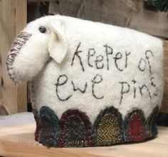 a sheep made out of wool with words on it's face and ears, sitting on a wooden shelf