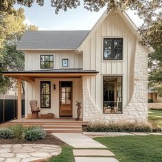 a white house with a black roof and two doors on the front porch is surrounded by green grass