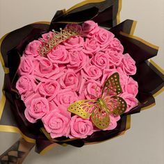 a bouquet of pink roses with a gold butterfly on the top and black ribbon around it