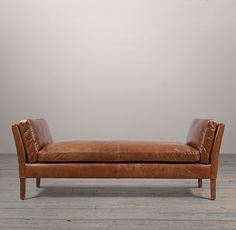 a brown leather chaise lounger sitting on top of a wooden floor next to a white wall