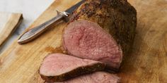 sliced meat sitting on top of a wooden cutting board with a knife next to it