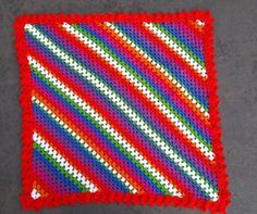 a crocheted red square with white and green stripes on it sitting on a gray surface