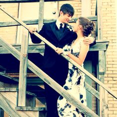 a man and woman in formal wear standing on stairs next to each other with their arms around each other