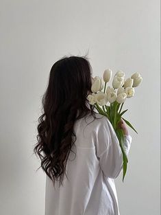 a woman holding a bouquet of white tulips in front of her face and back to the camera