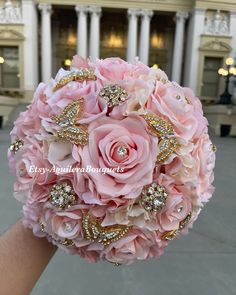 a bridal bouquet with pink roses and gold brooches in front of a building