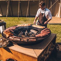 a man grilling meat on top of an open fire pit in the grass outside