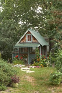 a small wooden house in the middle of some trees and flowers, with a pathway leading to it